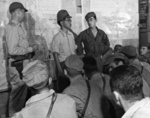 US Army Ground Liaison Officer Maj Mortimer H Jordan, left, Japanese POW 2Lt Minoru Wada, center, and interpreter Sgt Charles T Imai provide a briefing for the 1st Marine Air Wing fighter and bomber pilots, Aug 9, 1945