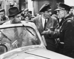 American photographer Julien Bryan (left, with fedora), through his interpreter (center, speaking), being questioned by Polish policeman Frank Kotlewski (right), Warsaw, Poland, 9 Sep 1939; the windshield was said to have been damaged by flying debris during a German air attack