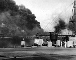 Smoke rising from Pearl Harbor’s Battleship Row as seen from the Submarine base, 7 Dec 1941, Pearl Harbor, Hawaii. Note submarine rescue ship USS Widgeon at right and buildings of the Supply Base beyond.