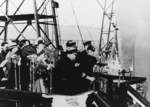 Josephine Doolittle, wife of James Doolittle, breaking a bottle of champagne at the launching ceremony of carrier Shangri-La, Norfolk Navy Yard, Portsmouth, Virginia, United States, 24 Feb 1944, photo 2 of 2; note yard commandant Rear Admiral Felix Gygax holding a microphone near the bottle