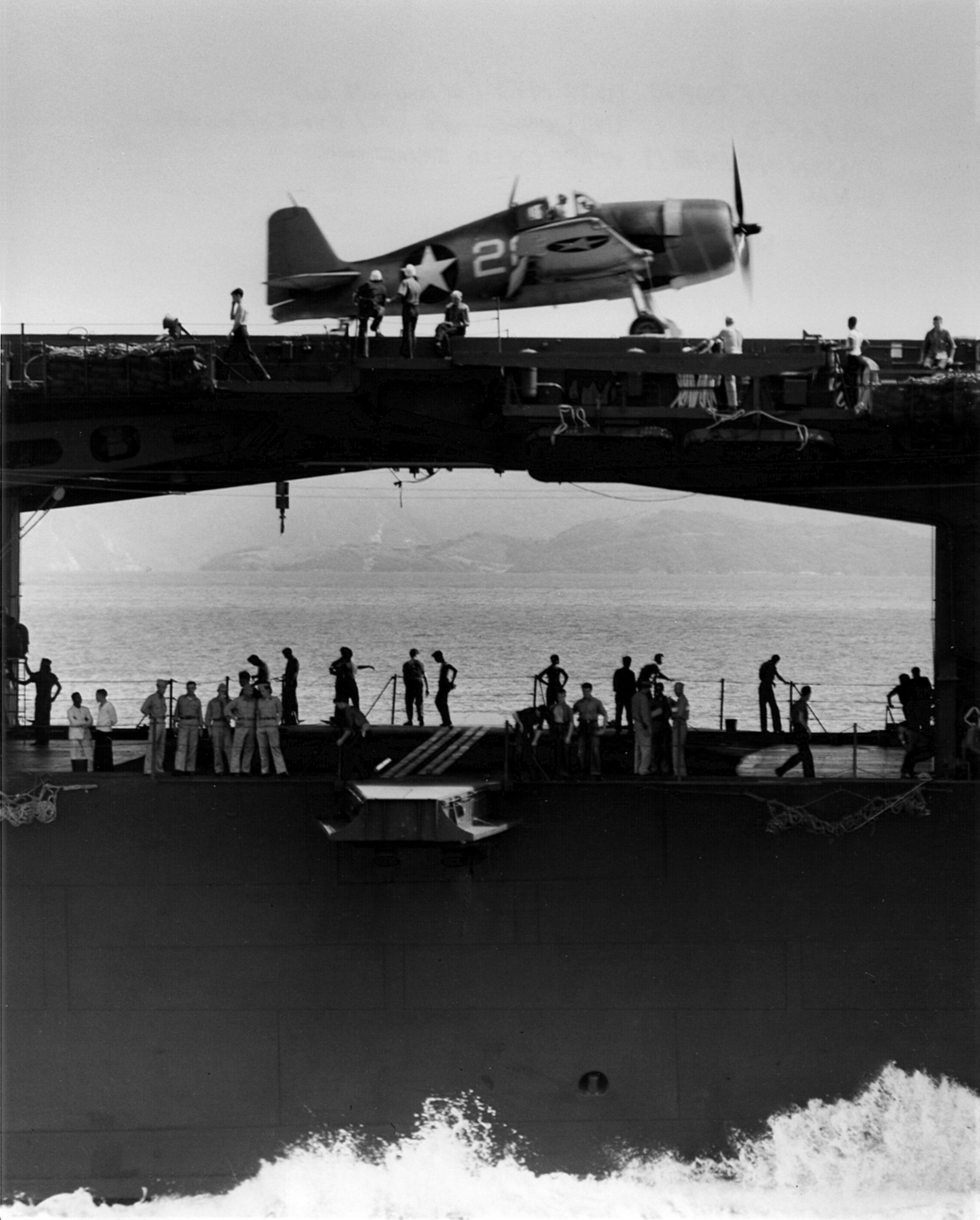 Starboard side view of the carrier Yorktown (Essex-class) with an F6F-3 Hellcat fighter of VF-1 on the fight deck above the athwartship hangar deck catapult, June 1943.