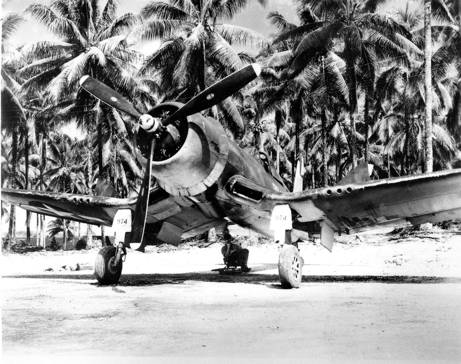 A crewman finds the only shade there is on the airstrip on Green Island (now Nissan Island), Northern Solomons, beneath an F4U-1D Corsair fighter of Marine Squadron 222, 1943-44.