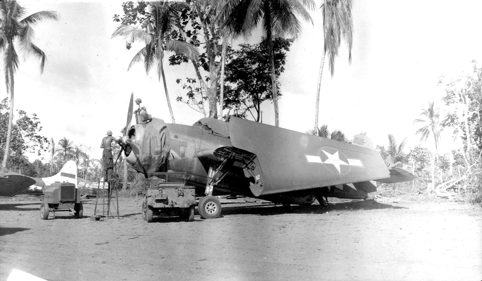 A Marine Corps TBM-1C Avenger of the 7th Fleet Command undergoing some maintenance at the Cyclops aerodrome, Hollandia, New Guinea, Jul-Aug 1943. Note the Jeep and the tail of an Army A-24 Banshee painted as a target tug.