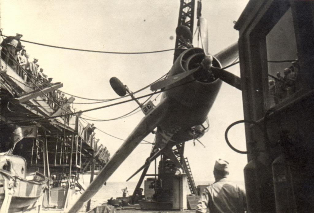 A damaged F6F Hellcat being hoisted by a crane from the training aircraft carrier USS Sable to a waiting barge on Lake Michigan, United States, 1945.