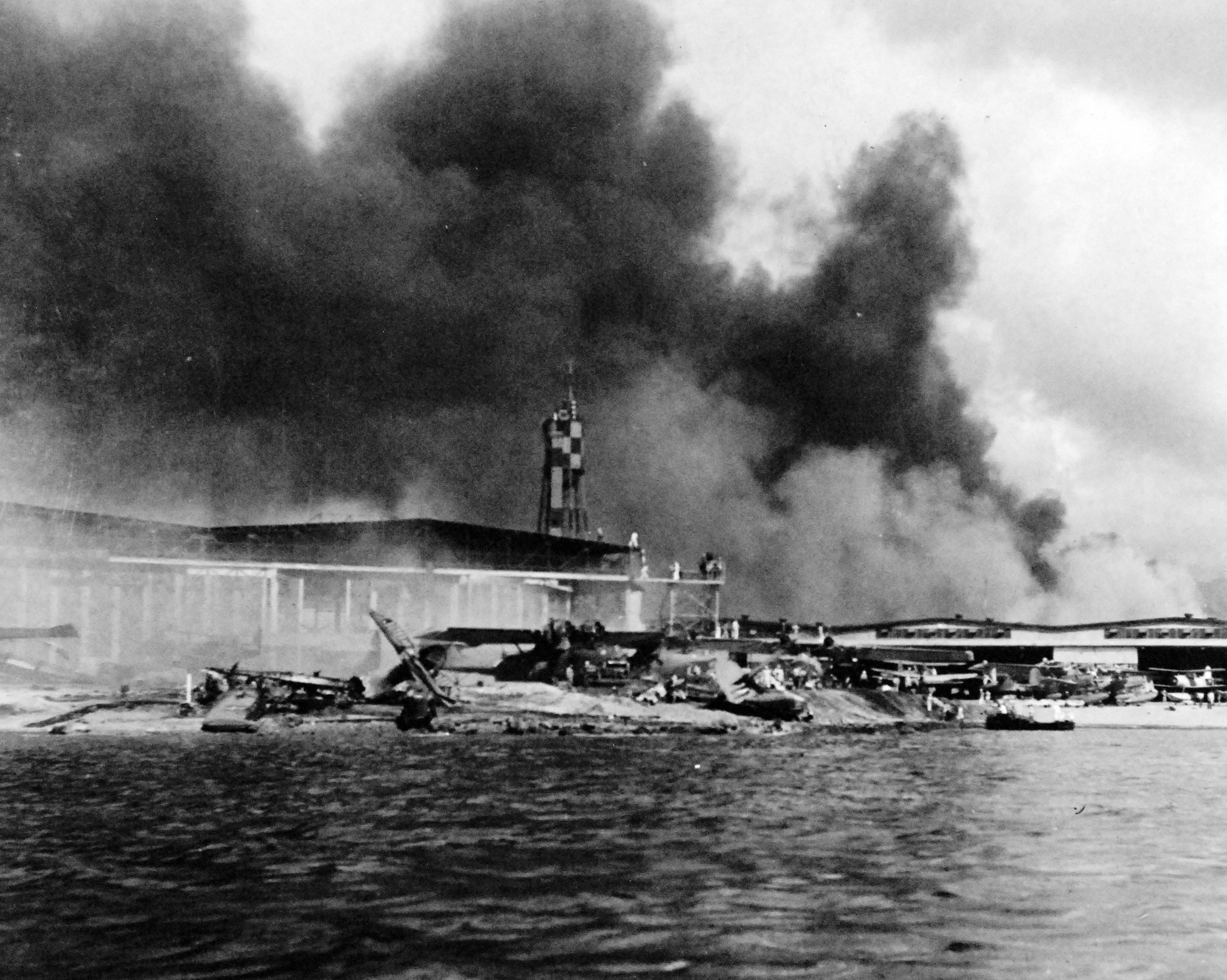 Damaged PBY Catalinas on the seaplane ramp of Ford Island, Pearl Harbor, Oahu, Hawaii, Dec 7, 1941. White smoke from burning hangars and black smoke from burning battleships is also visible.