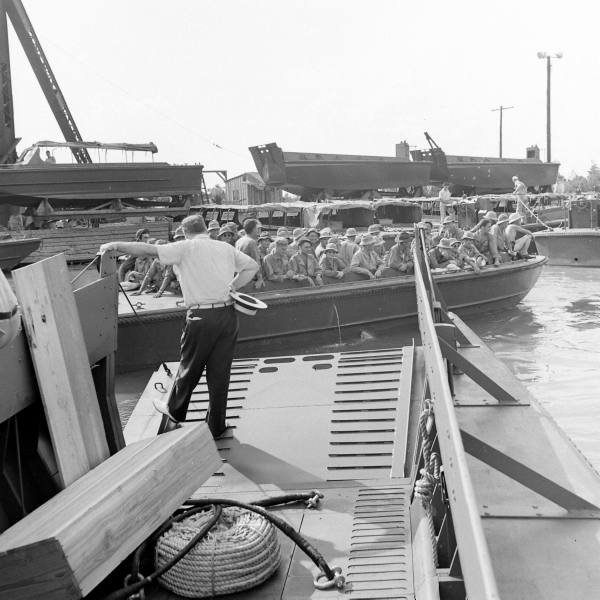Andrew Higgins standing on the bow ramp of an LCVP prototype observing an exercise with a loaded Eureka Boat (predecessor of the LCP(L)), New Orleans, Louisiana, United States, circa 1941. Note other boats on the wharf.
