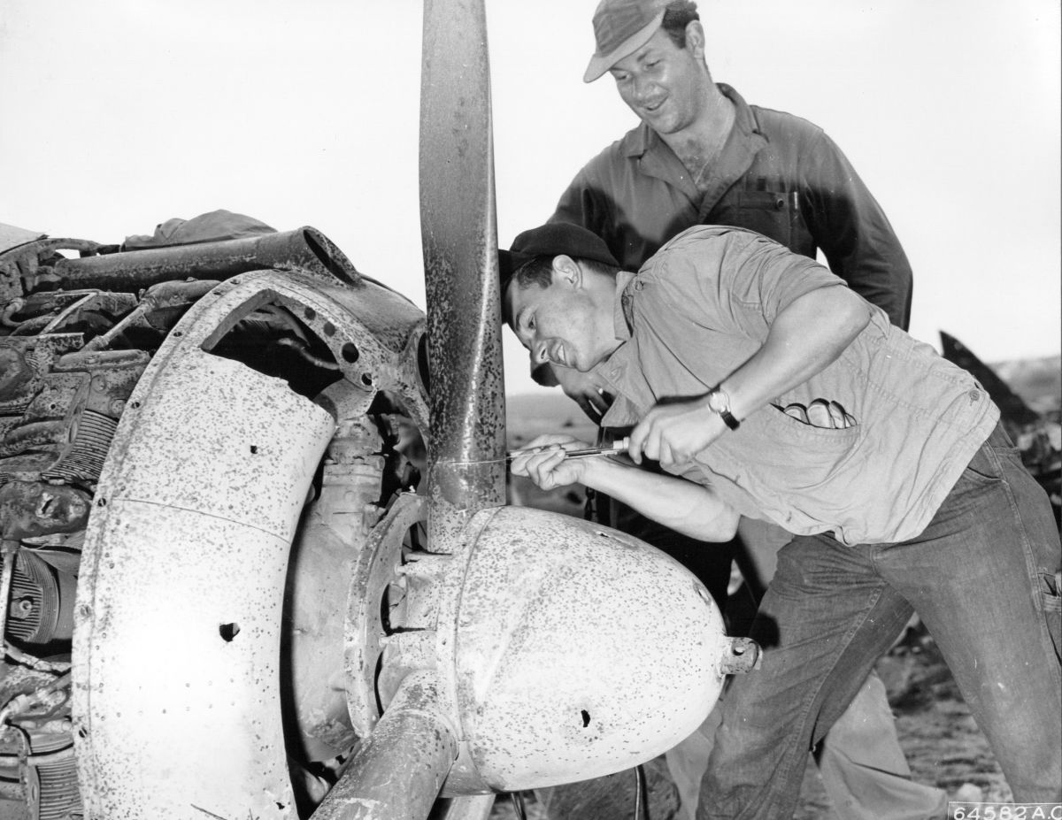 Souvenir hunters on Iwo Jima sawing the propeller off of a wrecked Japanese Nakajima Ki-43 