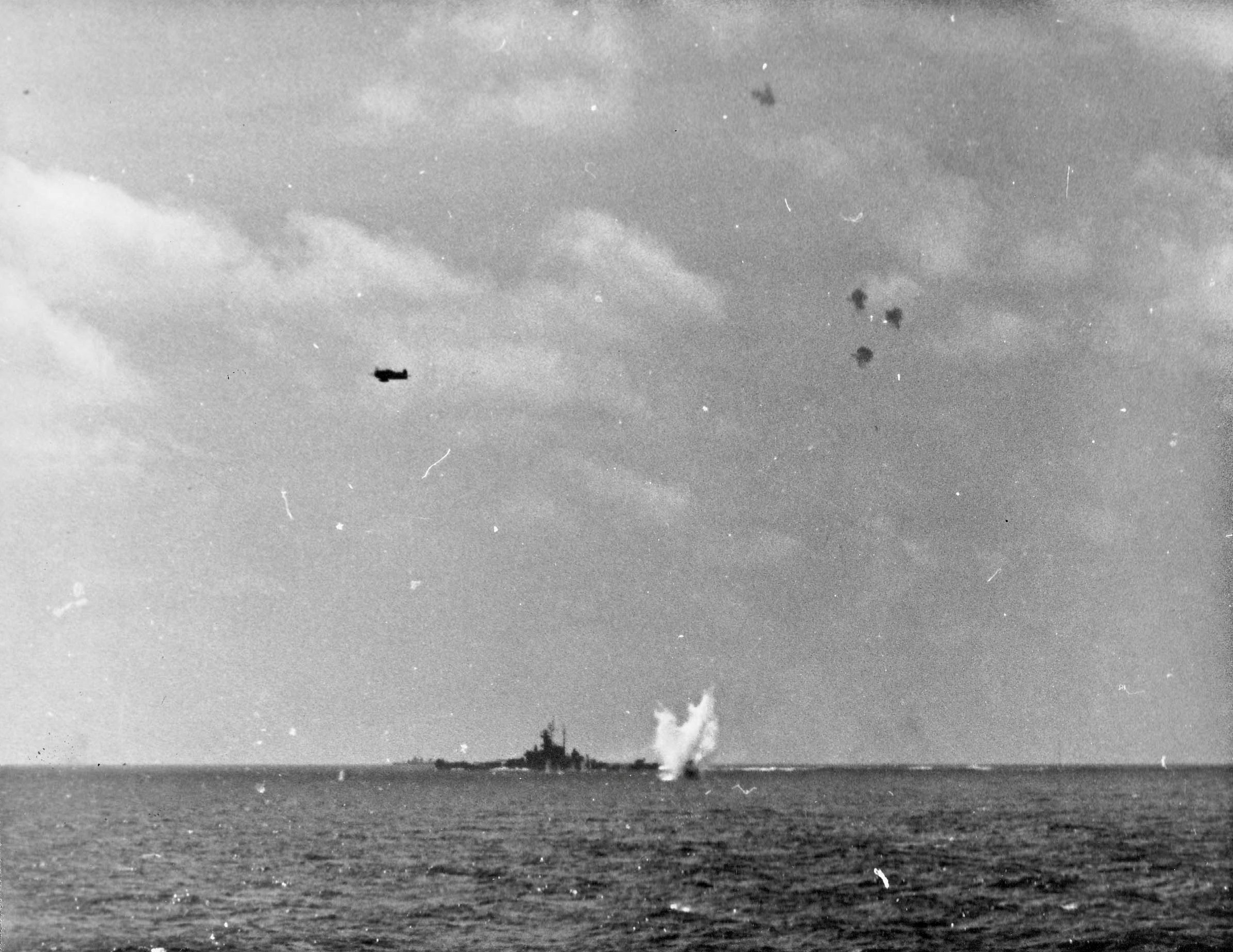 A Japanese D4Y Suisei fighter splashing into the sea after being shot down during an attack on the American fleet as seen from USS Essex, 25 Nov 1944. Note battleship USS South Dakota and US fighter in level flight