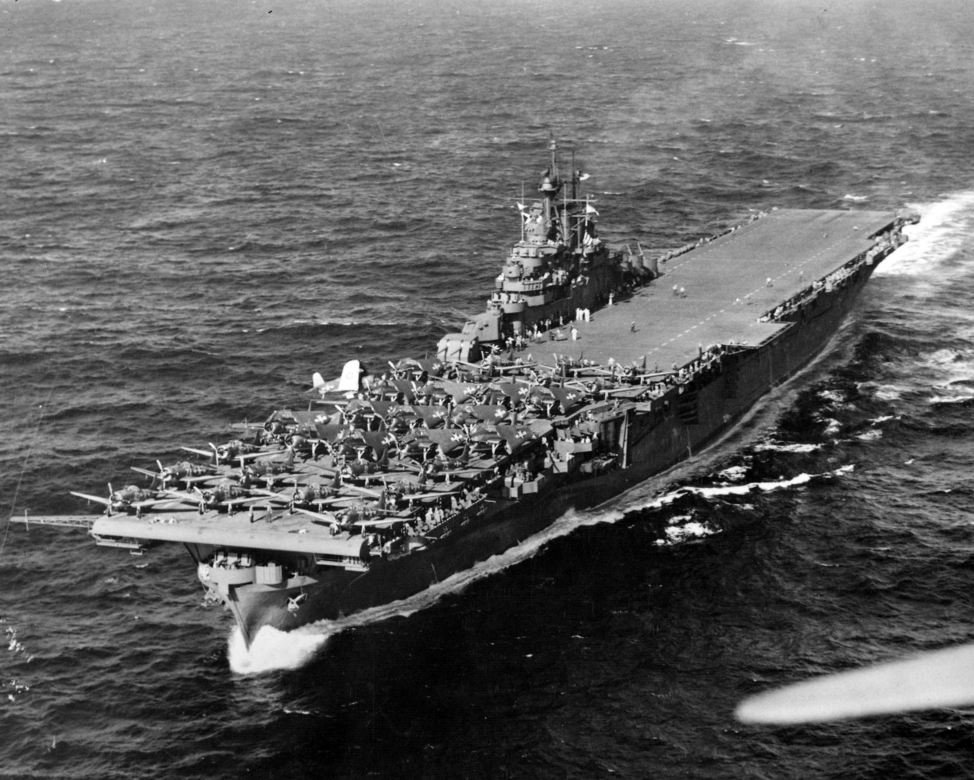USS Intrepid under way 26 Jan 1944 on her way to launch strikes against Truk Atoll (now Chuuk). Note the forward flight deck filled SBD Dauntless and TBF Avenger aircraft and one F4U Corsair on the outrigger sponson.