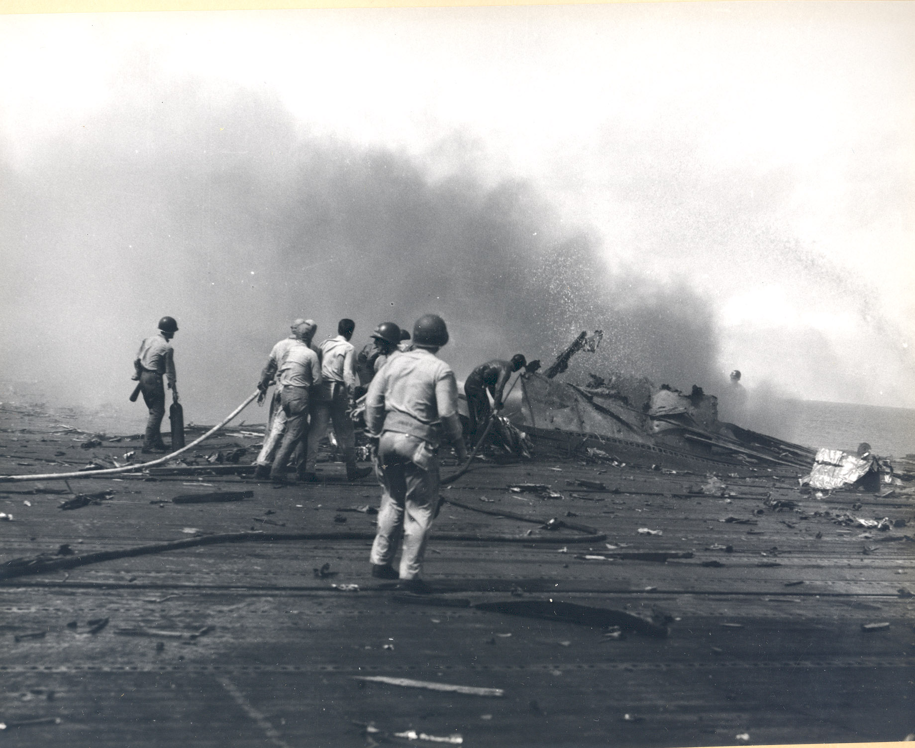 Damage control parties trying to bring fires under control on the flight deck of USS Intrepid following the crash of a Japanese special attack aircraft off the Philippines, 25 Nov 1944. Note the bulge in the deck
