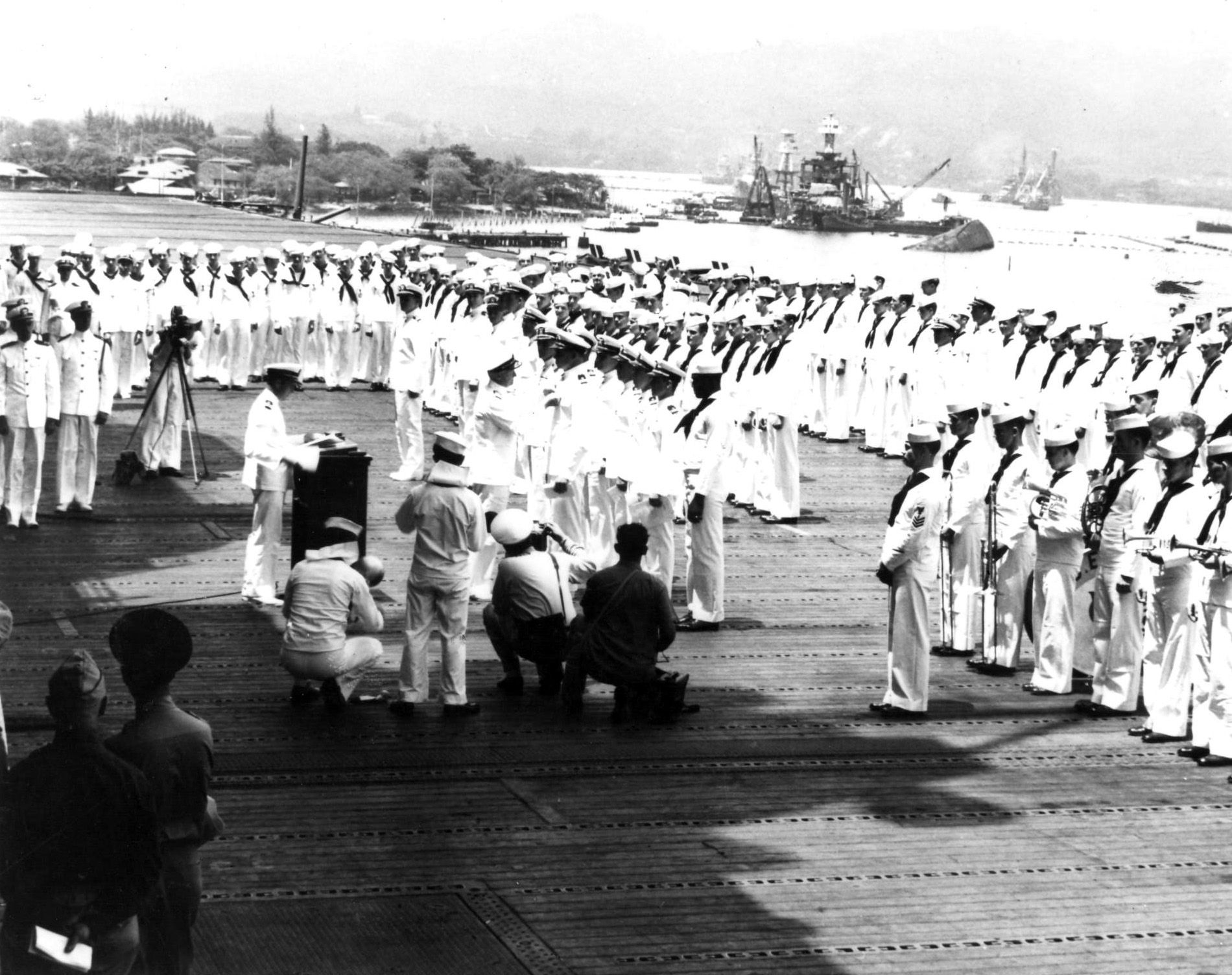 Admiral Chester Nimitz aboard USS Enterprise to present awards, Pearl Harbor, Territory of Hawaii, 27 May 1942. Note capsized USS Oklahoma and sunken USS West Virginia and USS Arizona in the background.