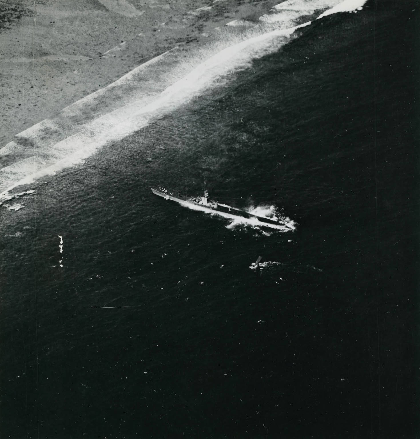 Submarine USS Harder with her bow against the reef off Woleai, Caroline Islands, 1 Apr 1944 as a rescue party went ashore to rescue aviator Ensign John Galvin on the beach. Note SOC Seagull seaplane.