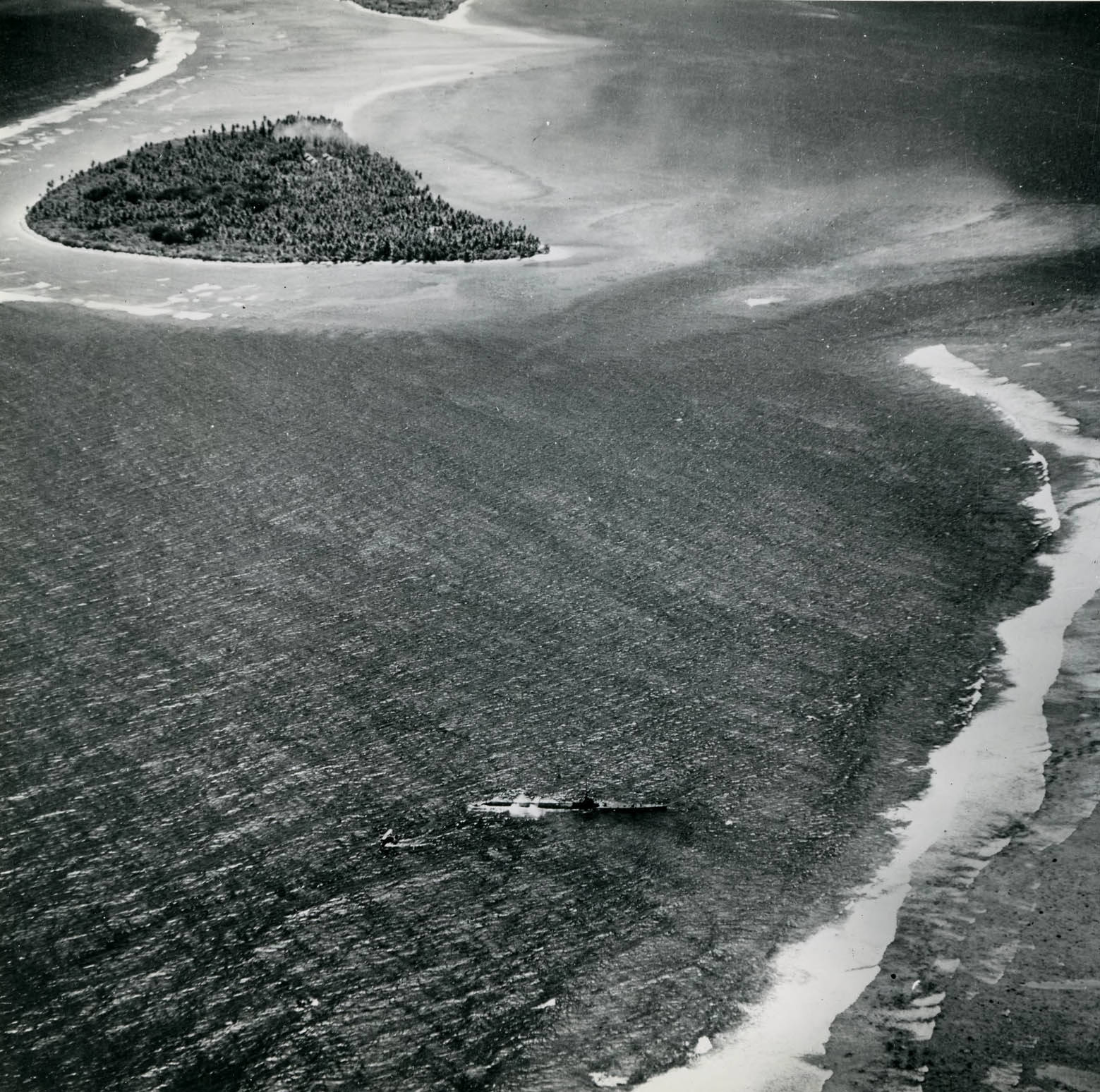 Submarine USS Harder backing away from the reef off Woleai, Caroline Islands, 1 Apr 1944; note SOC Seagull seaplane off Harder’s starboard quarter and rescued aviator Ensign John Galvin in a raft off the bow.