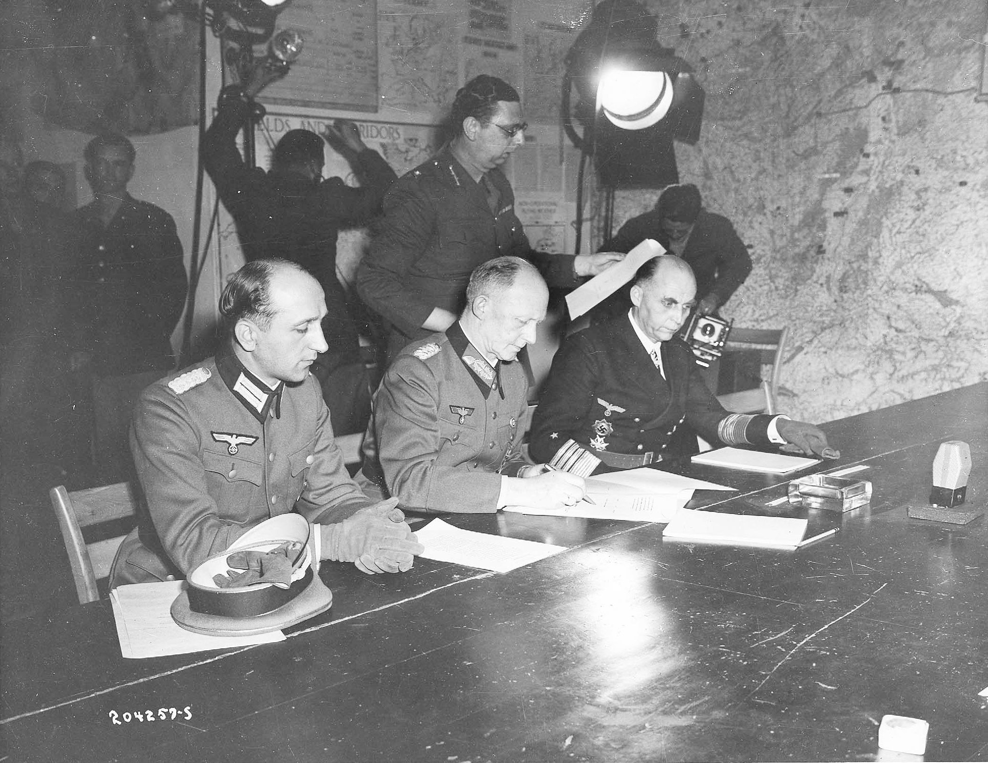Jodl signing surrender documents at Eisenhower's headquarters, flanked by Major Wilhelm Oxenius and Admiral Hans-Georg von Friedeburg, Reims, France, 7 May 1945, photo 4 of 4