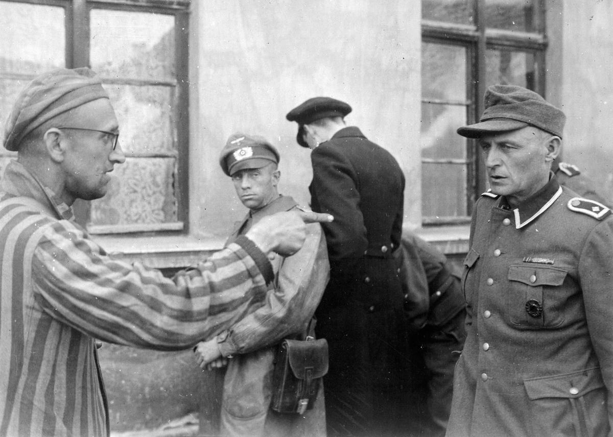 After being liberated by the US 1st Army, a Russian prisoner points out one of the particularly brutal guards at Buchenwald, Germany, 14 Apr 1945. Note guard’s black wound badge indicating he is combat wounded.