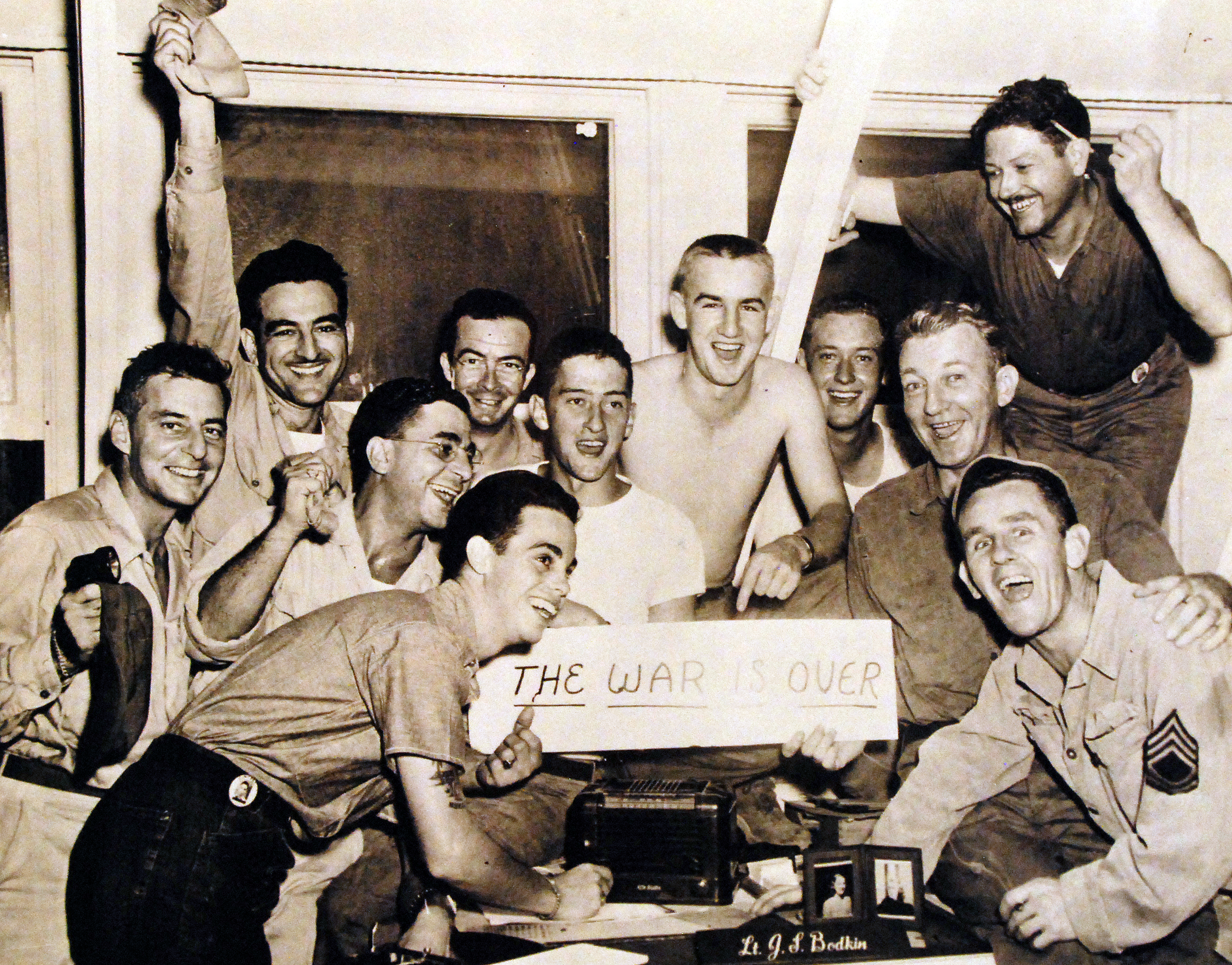 Carl Gurtcheff, Vic Colucci, Arthur Ryding, Clifford Martin, William Reigger, James Badgett, J. F. Whitely, Dan Brown, Clayton Aylor, and Denny O'Neill celebrating victory at CINCPAC headquarters in Guam, 15 Aug 1945