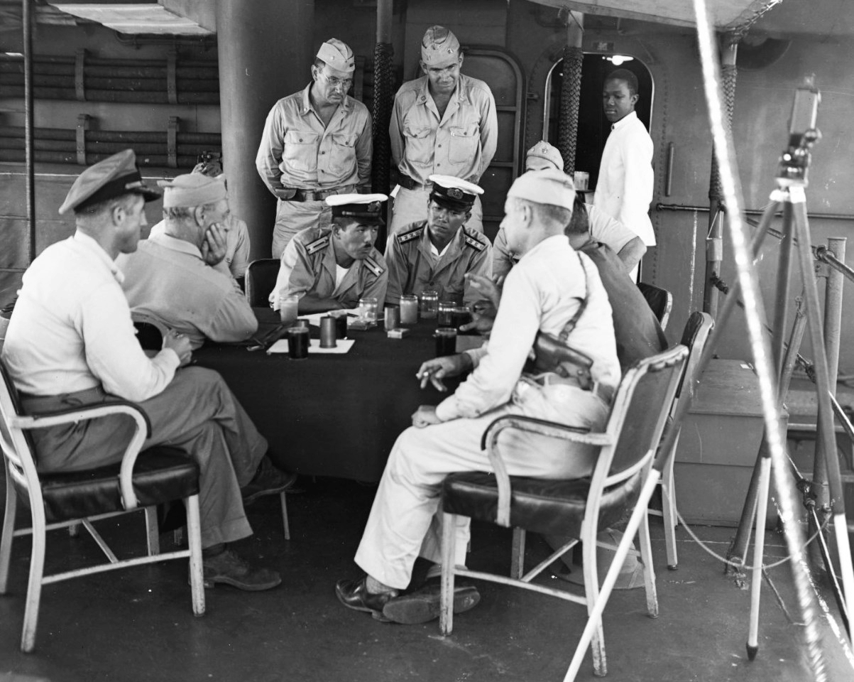 Surrender negotiations at Mili Atoll, Marshall Islands, aboard USS Levy, 19 Aug 1945; L to R: Cdr H.E. Cross, Majuro commander Capt H.B. Grow, LtCdr Toyda and Lt Hutsu, Lt Col G.V. Burnett (only cap showing), and others