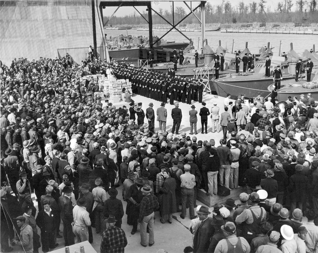 Commissioning ceremonies for Motor Torpedo Boat Squadron 16 (MTBRon 16) at Higgins Boatworks in New Orleans, Louisiana, United States, 26 Feb 1943. Note Higgins 78-foot PT Boats and LCM landing craft in the distance.