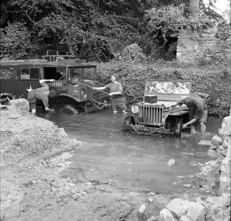 British soldiers wash a Canadian-built CMP command car and an American-built Jeep in a local stream in Normandy, France, 5 Jul 1944.