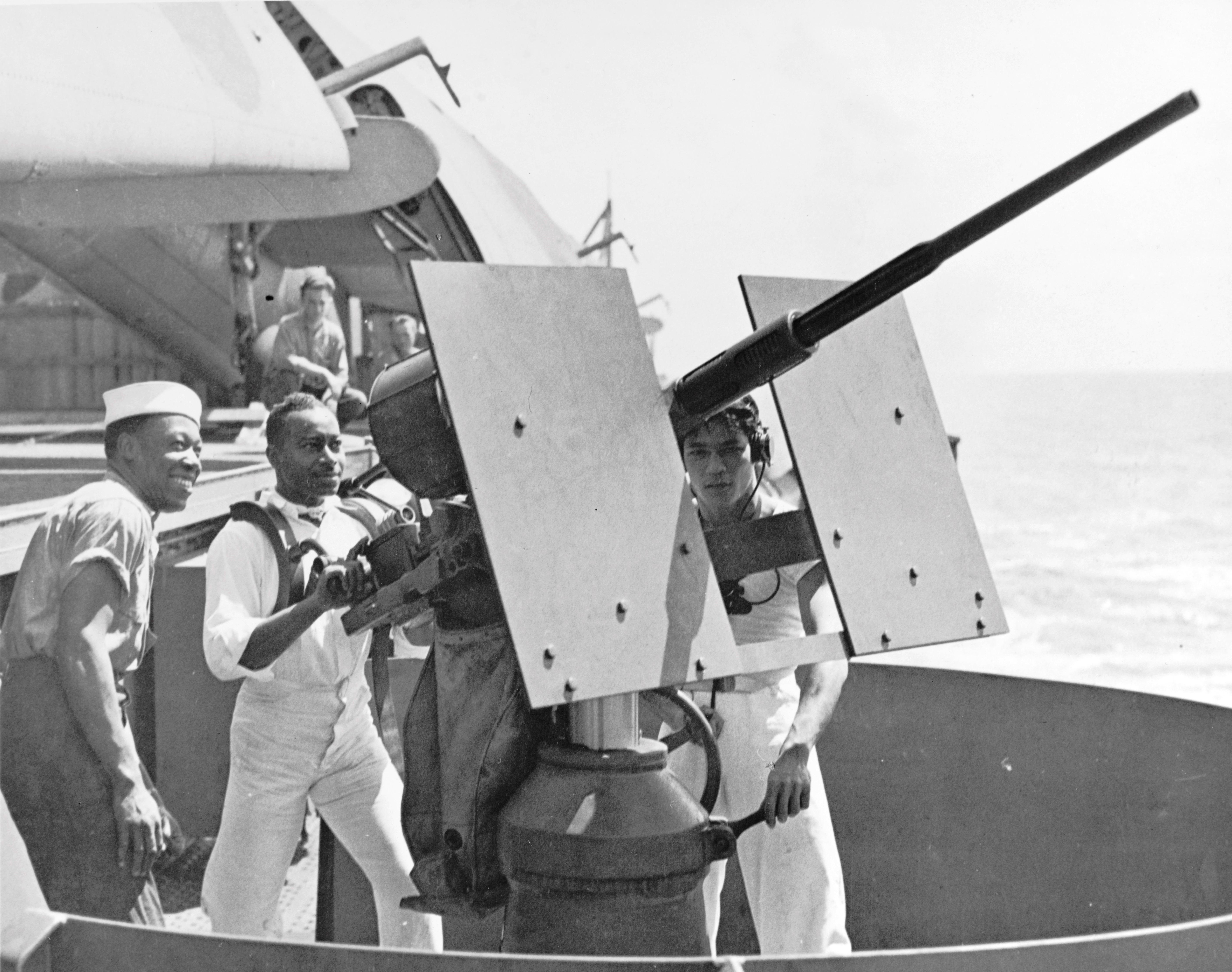 African-American mess attendants take their turn at a 20mm gun during gunnery training on Aircraft Transport USS Copahee during transit from California to Pearl Harbor, 9 Sep 1942. Note TBF Avengers on the flight deck.