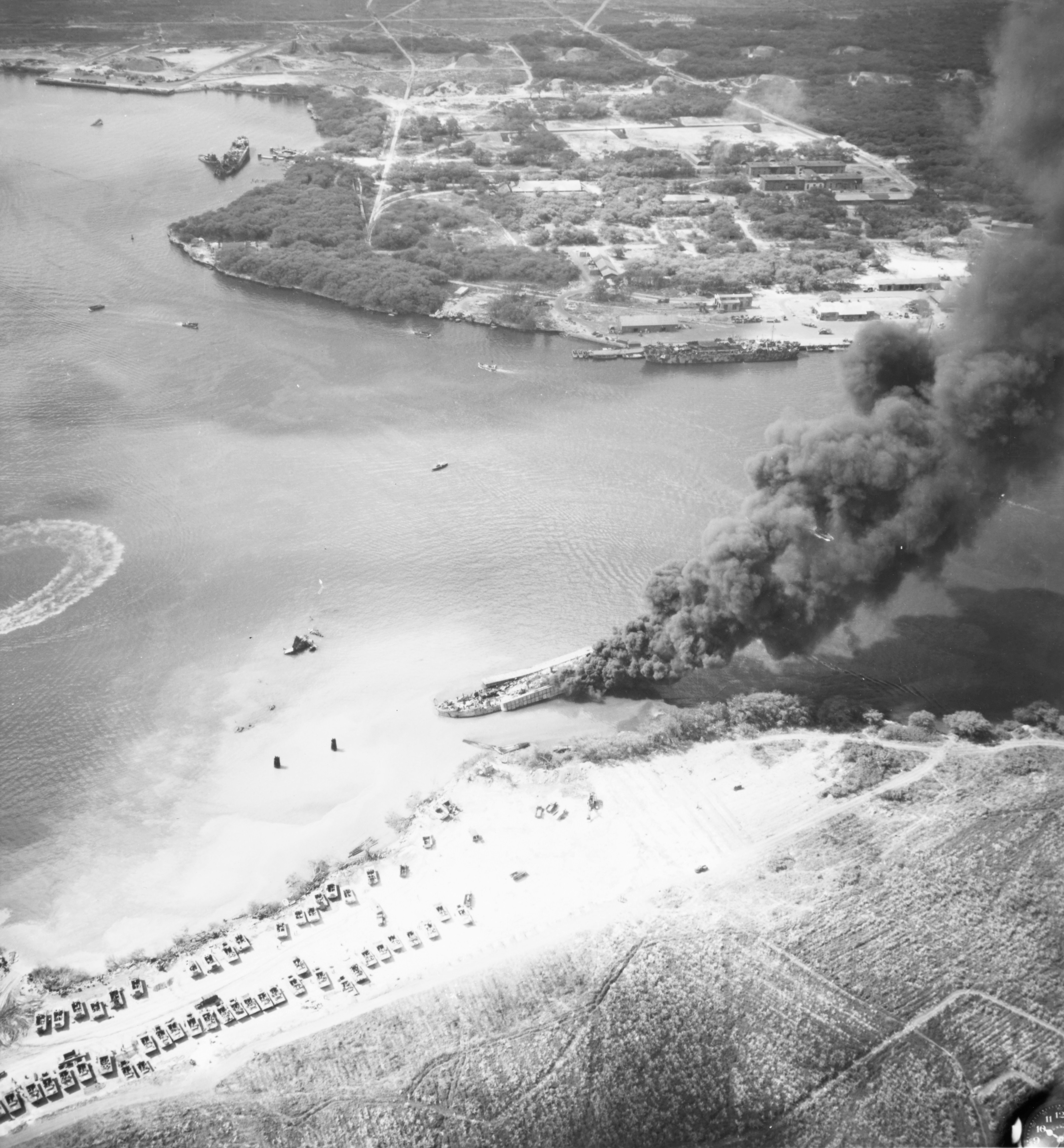 LST-480 burning in West Loch, Pearl Harbor, Hawaii, 23 May 1944 two days after the West Loch explosion that sank six LSTs. The chain-reaction explosion started on LST-39 whose wreckage is visible off LST-480’s bow.