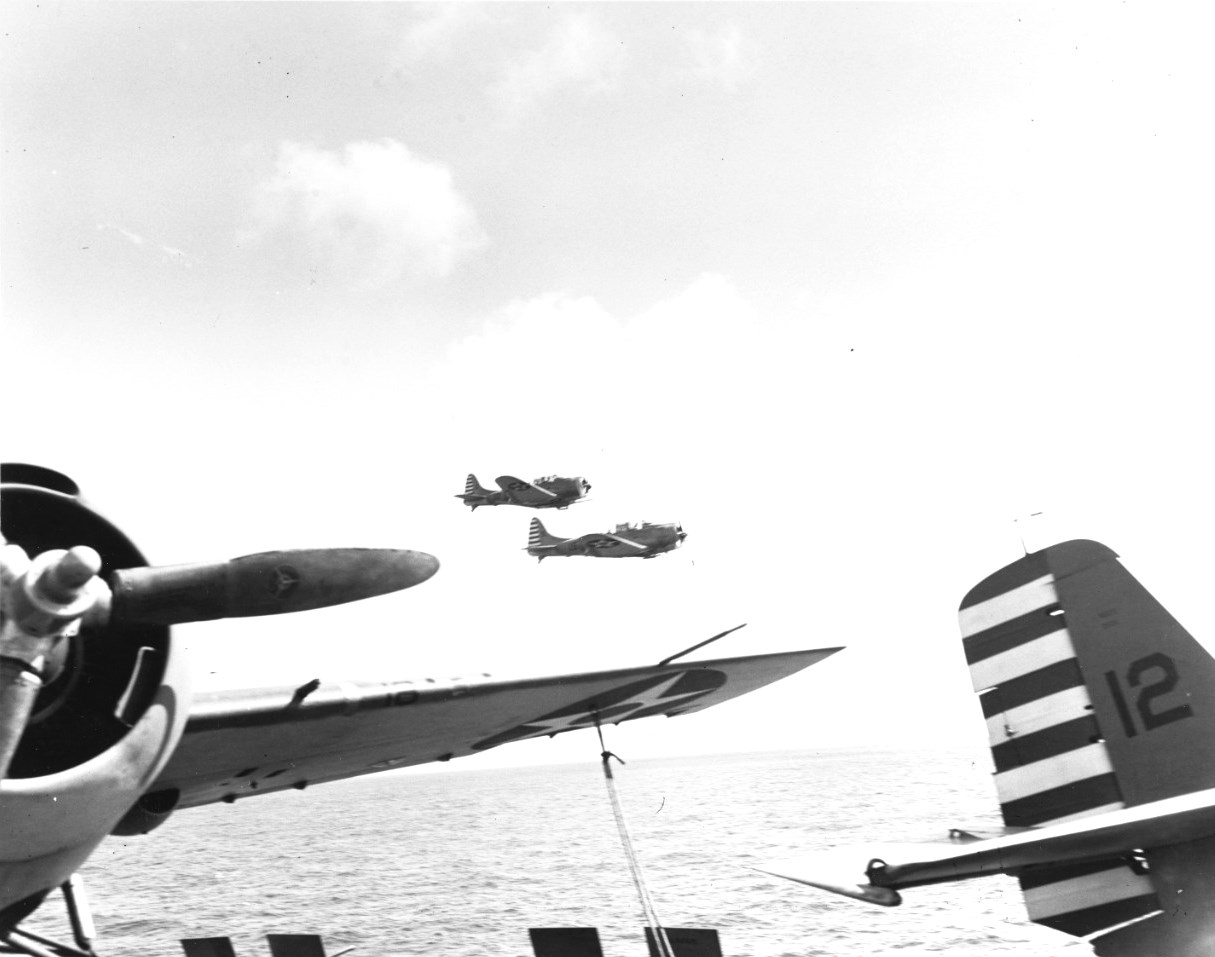 Two SBD-3 Dauntless dive bombers of Scouting Squadron 5 flying by USS Yorktown (Yorktown-class) in the Coral Sea, Apr 1942. Note F4F-3 Wildcats of Fighting Squadron 42 and red & white rudder stripes in use only 4 months