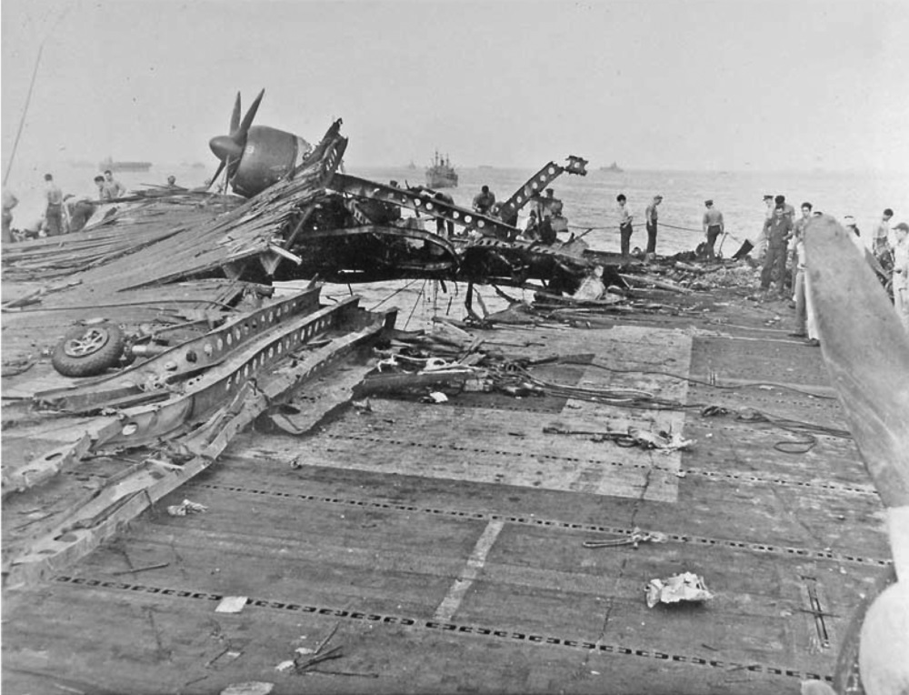 What is left of an SB2C Helldiver on the heavily damaged flight deck of the USS Randolph after a P1Y Ginga special attack bomber crashed into the ship while at anchor in Ulithi Lagoon, Caroline Islands, 11 Mar 1945.