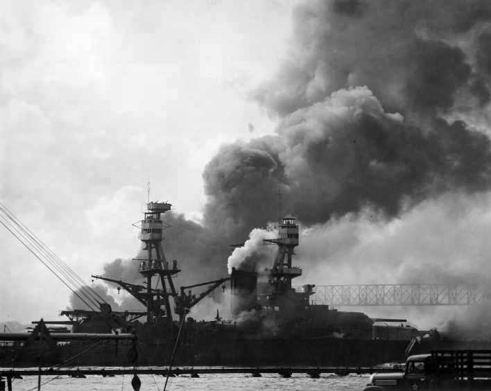 USS Nevada moving down the channel during the Japanese air attack on Pearl Harbor, Hawaii, 7 Dec 1941. Note smoke from USS Cassin and USS Downes and also the Gantry Crane spanning the drydocks.