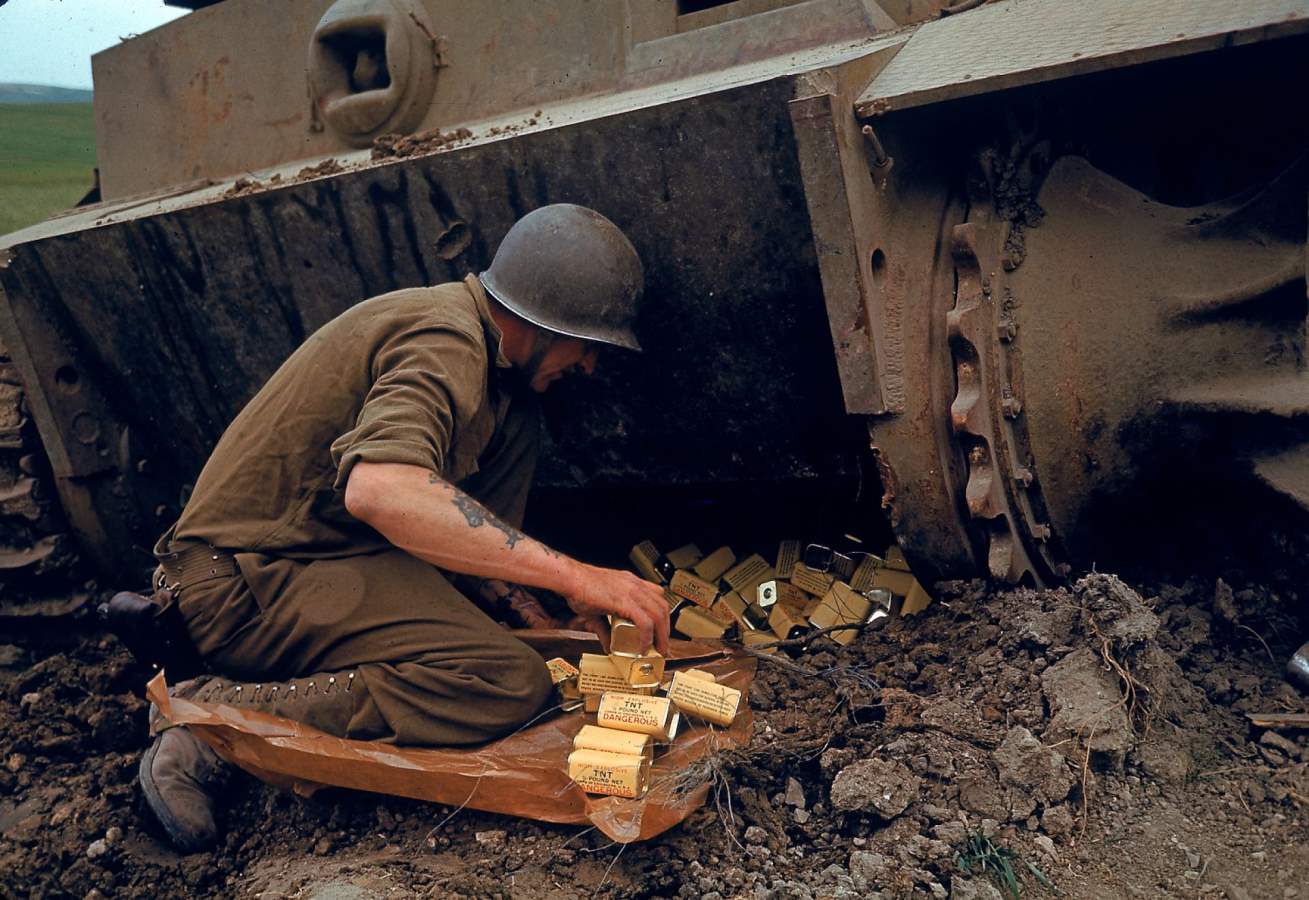 United States Army combat engineer placing several half-pound cans of TNT explosive under an abandoned German tank during the Battle of El Guettar, Tunisia, Apr 1943.