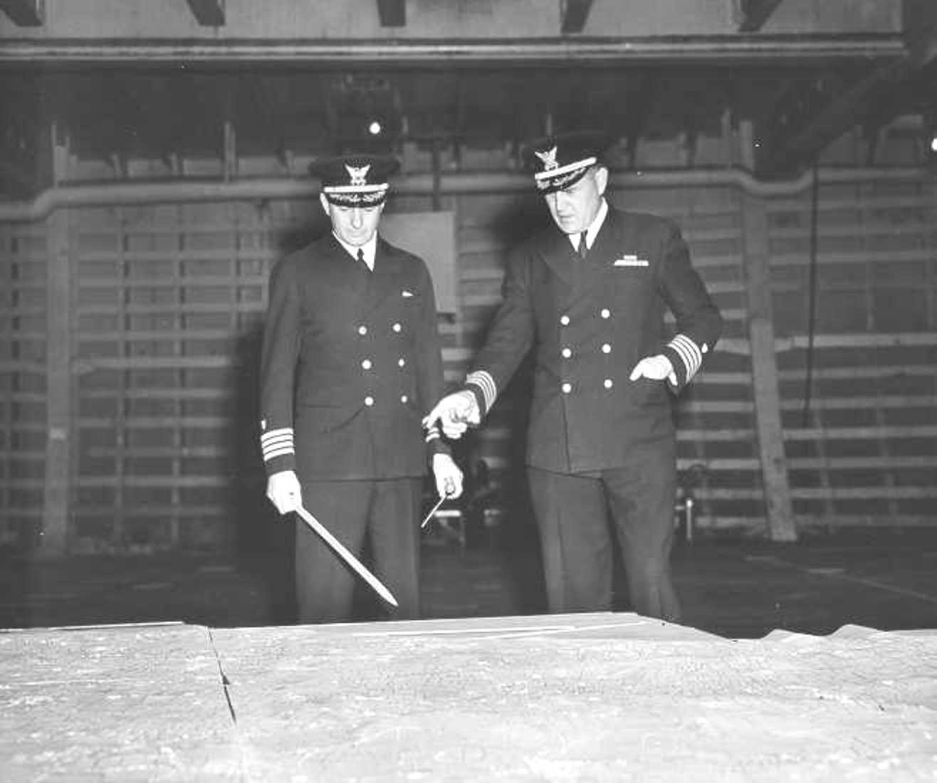 United States Coast Guard Captains Edward Fritzche (left) and Miles Imlay (right) examining a relief map of Omaha Beach laid out in the hold of the Attack Transport USS Samuel Chase, Jun 1944.