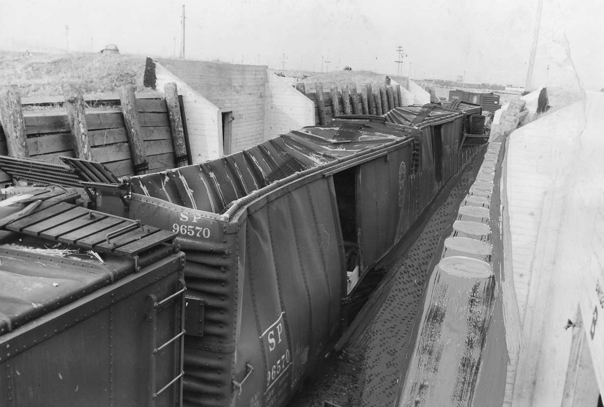 Damaged railroad cars loaded with munitions in a revetment at Port Chicago, California, United States that were caved in by a massive explosion the night before, 18 Jul 1944.