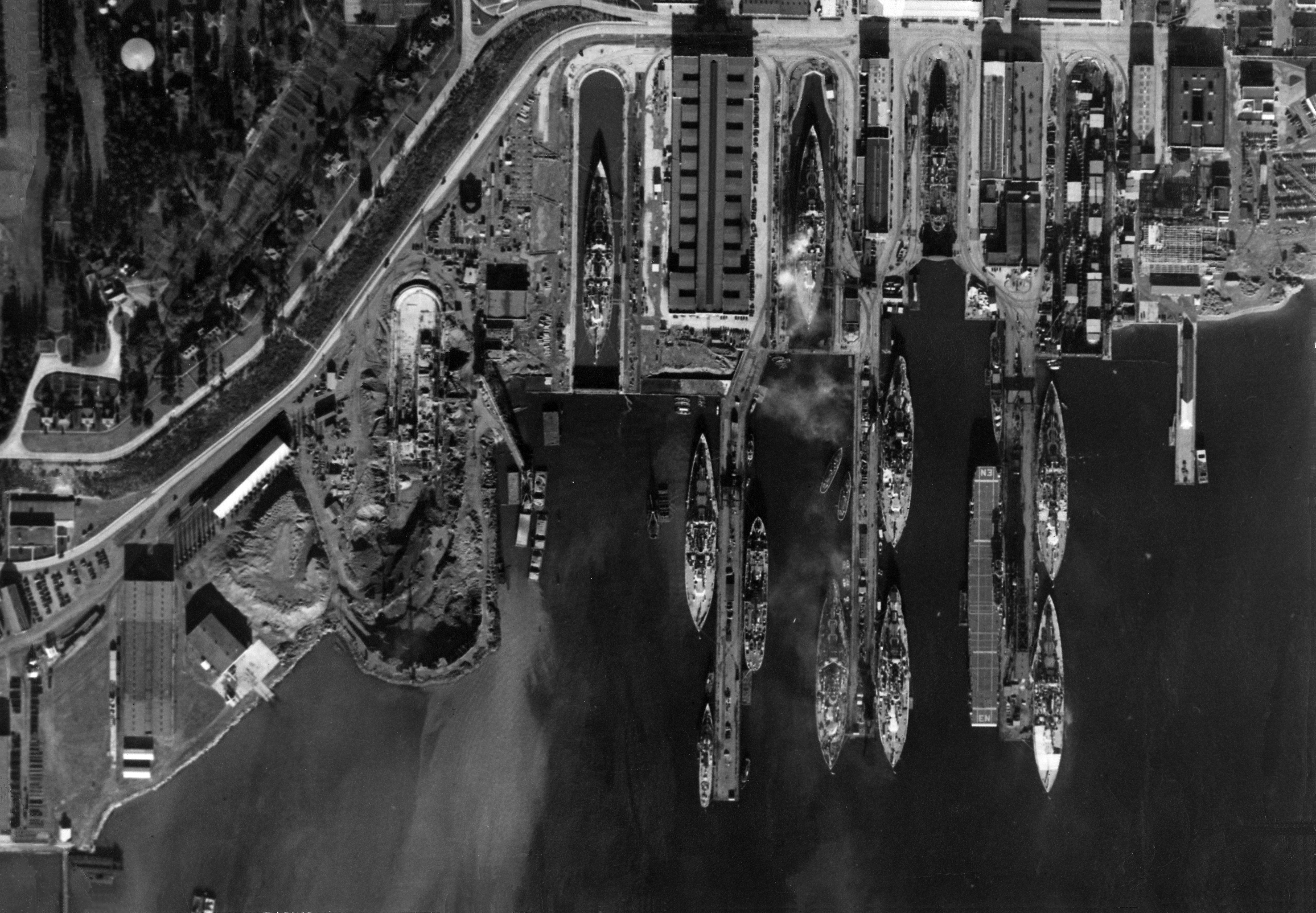 Straight down aerial view of the piers and drydocks at the Puget Sound Naval Shipyard, Bremerton, Washington, United States full of battleships and one carrier, USS Enterprise, 1940.