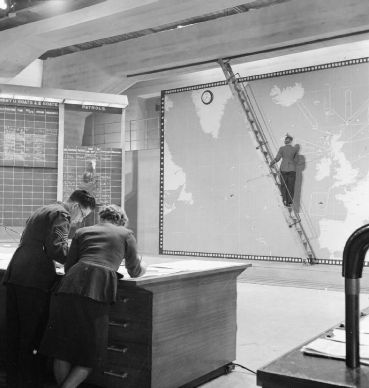 Sergeant Holland speaking with Section Officer Bewkey while Corporal Tomkinson places markers on a wall map and Aircraftwoman Tarrant recorded data on a chalkboard, on set of film Coastal Command, Pinewood Studios, Iver Heath, England, United Kingdom, 1942