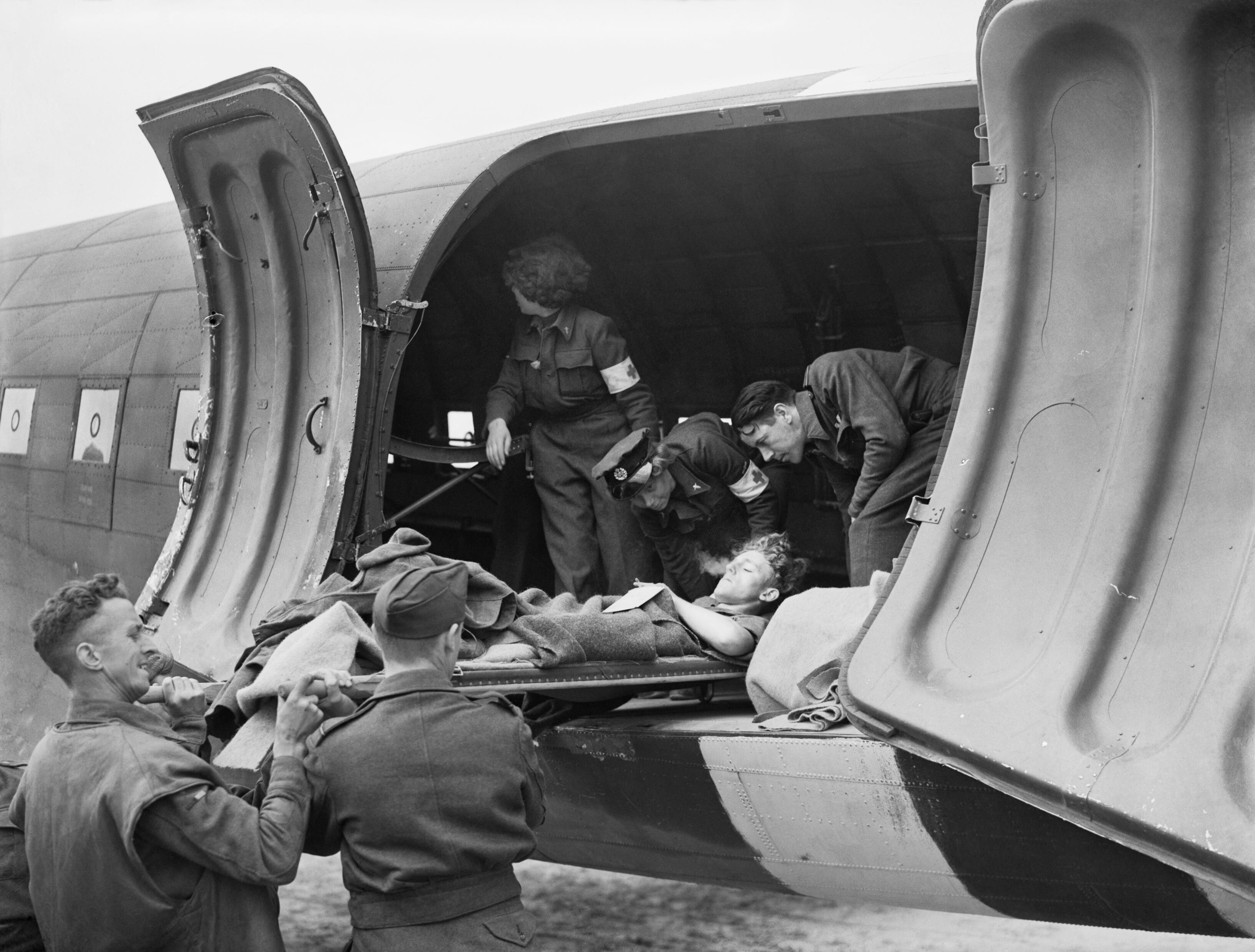 RAF air crew and WAAF nursing orderlies loading a wounded serviceman onto a Dakota Mark III aircraft of No. 233 Squadron RAF at B-2 Bazenville Advanced Landing Ground, Basse-Normandie, France, mid-Jun 1944