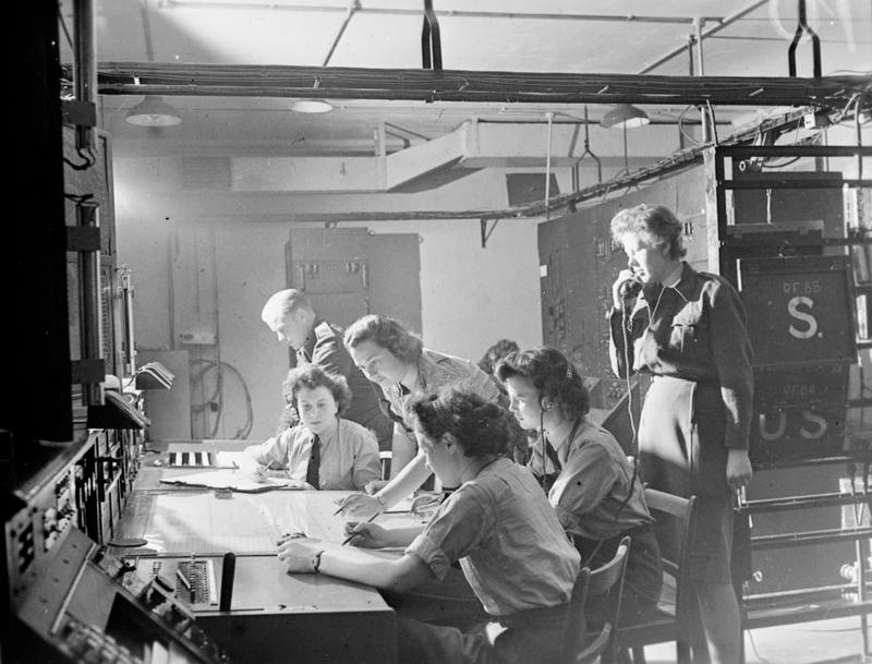 Flight Officer P. M. Wright supervising Sergeant K. F. Sperrin and WAAF operators Joan Lancaster, Elaine Miley, Gwen Arnold, and Joyce Hollyoak in the receiver room at RAF Bawdsey, Suffolk, England, United Kingdom, date unknown