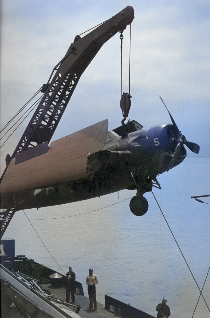 A damaged FM-2 Wildcat being hoisted by a crane from the training aircraft carrier USS Sable to a waiting barge on Lake Michigan, United States, 1943-45. [Colorized by WW2DB]