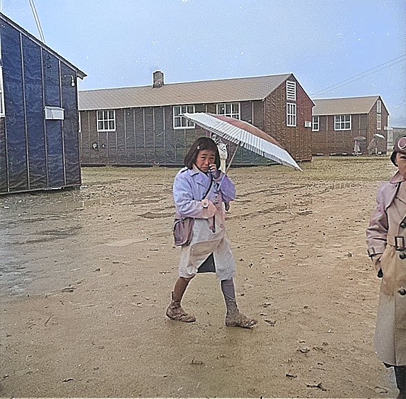 Japanese-American girl walking in rain, Jerome Relocation Center, Denson, Arkansas, United States, 12 Mar 1943 [Colorized by WW2DB]