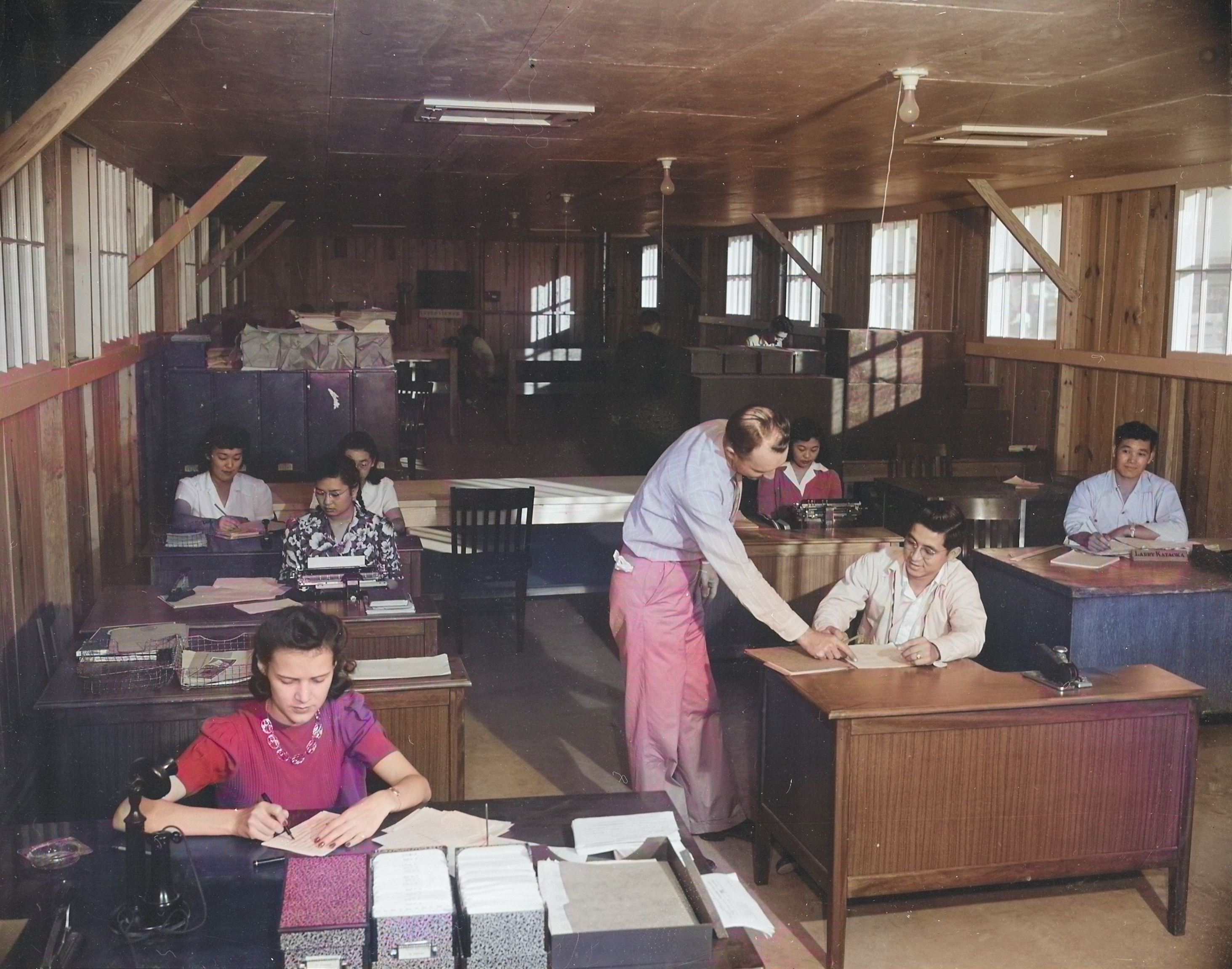Virginia Shilby (foreground left), John Tucker (center), and other workers at the Housing Department office of Jerome War Relocation Center, Arkansas, United States, 17 Nov 1942 [Colorized by WW2DB]
