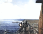 View of the USS Intrepid flight deck looking aft down the catwalk from the No. 4 5-inch gun mount, 1944-45. Note the arresting cables across the flight deck. Note also the anti-aircraft bursts on the horizon.