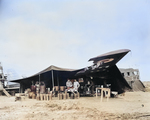 Lieutenant E. T. McBoon, Sergeant C. W. Moore, and Corporal William G. Warrington at a US field kitchen constructed under the wing of a damaged MB.200 bomber, North Africa, 1943