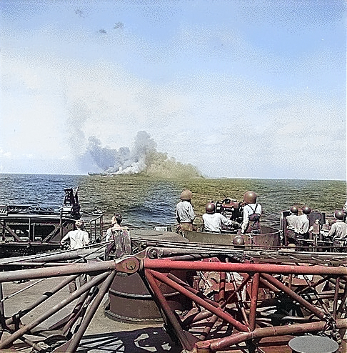 Intrepid smoking after being hit by Japanese special attack aircraft, seen from battleship New Jersey, 25 Nov 1944; note New Jersey's 40mm guns in foreground [Colorized by WW2DB]