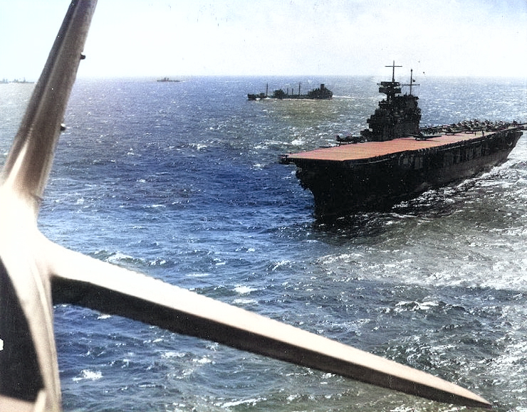 USS Yorktown seen from a TBD-1 aircraft, Pacific Ocean, Apr 1942; note F4F-3 Wildcat fighter preparing for takeoff, and fleet oiler USS Guadaloupe, a destroyer, and a cruiser just beyond [Colorized by WW2DB]