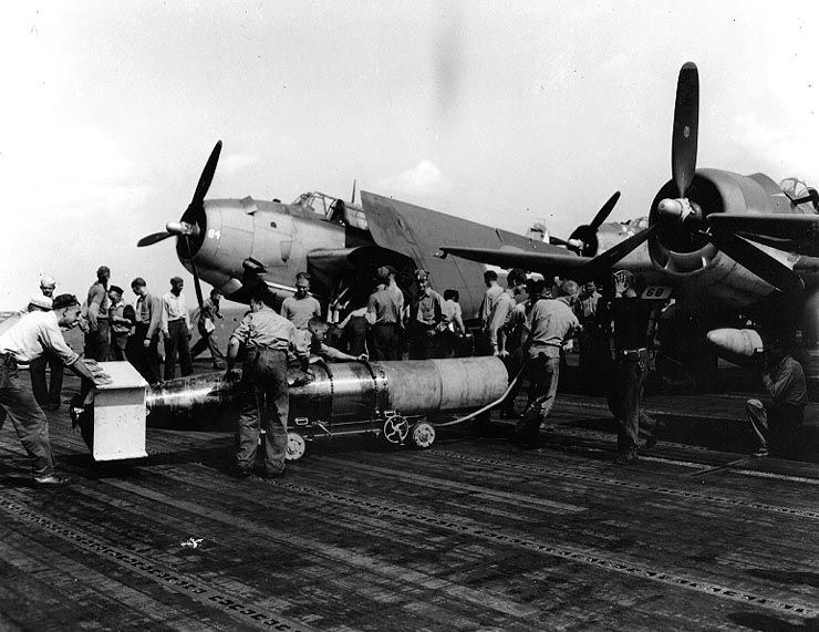 Flight deck crews of USS Wasp preparing a plywood-shrouded Mark XIII torpedo for a TBM Avenger aircraft for strikes in Taiwan-Philippine area, 13 Oct 1944; note TBM-1C Avenger and F6F-5 Hellcat