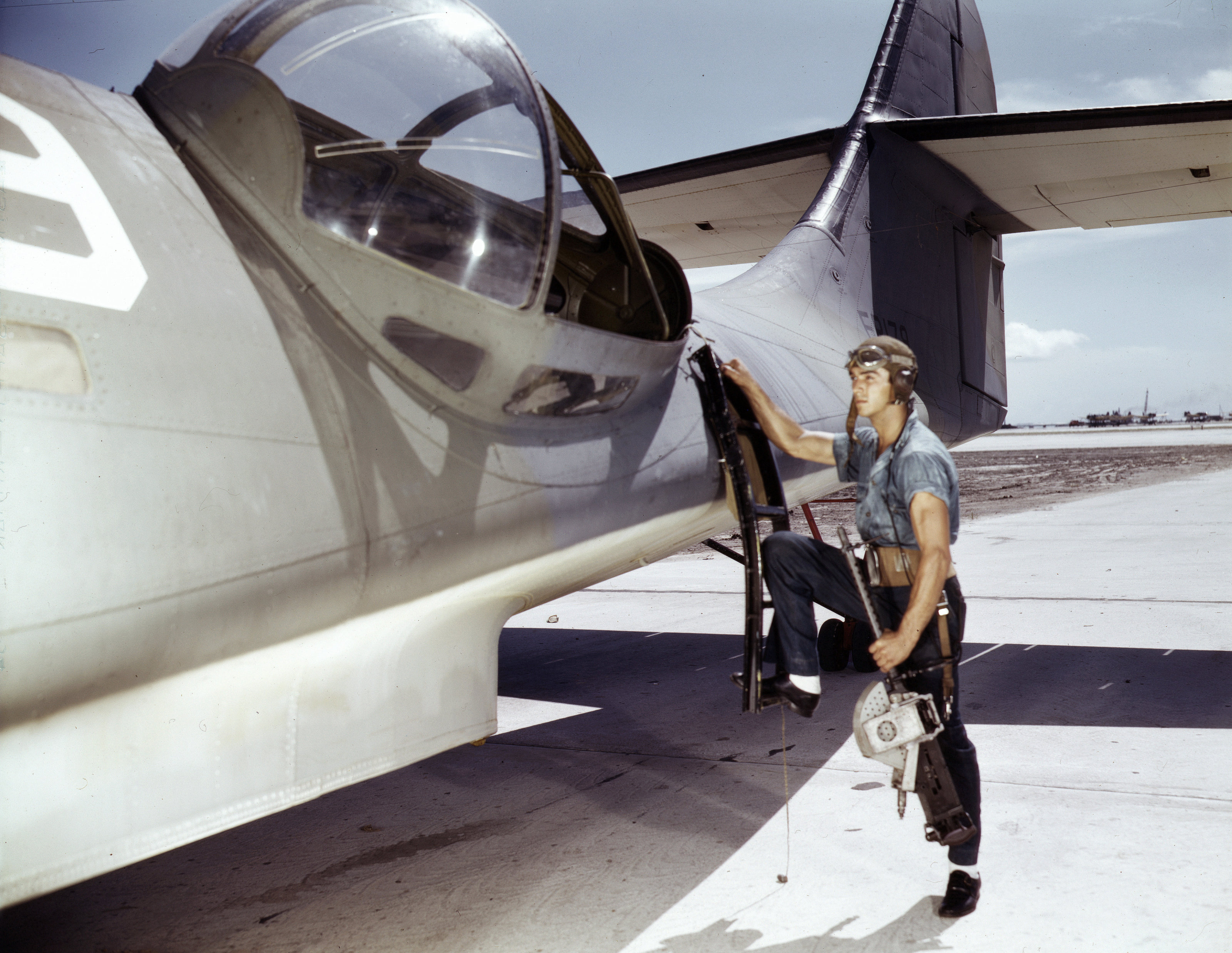 US Navy ordnanceman Jesse Rhodes Waller posing with a M1919 Browning machine gun next to a PBY Catalina aircraft, Naval Air Station, Corpus Christi, Texas, United States, Aug 1942, photo 1 of 3