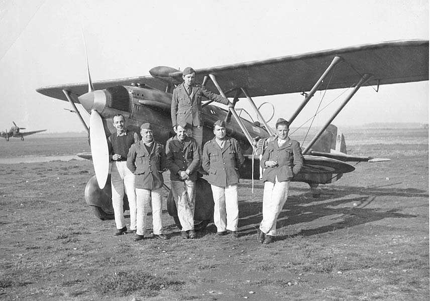 Italian Air Force personnel posing before a CR.32 biplane fighter, circa 1940-1942; note Ju 87 Stuka dive bomber in background