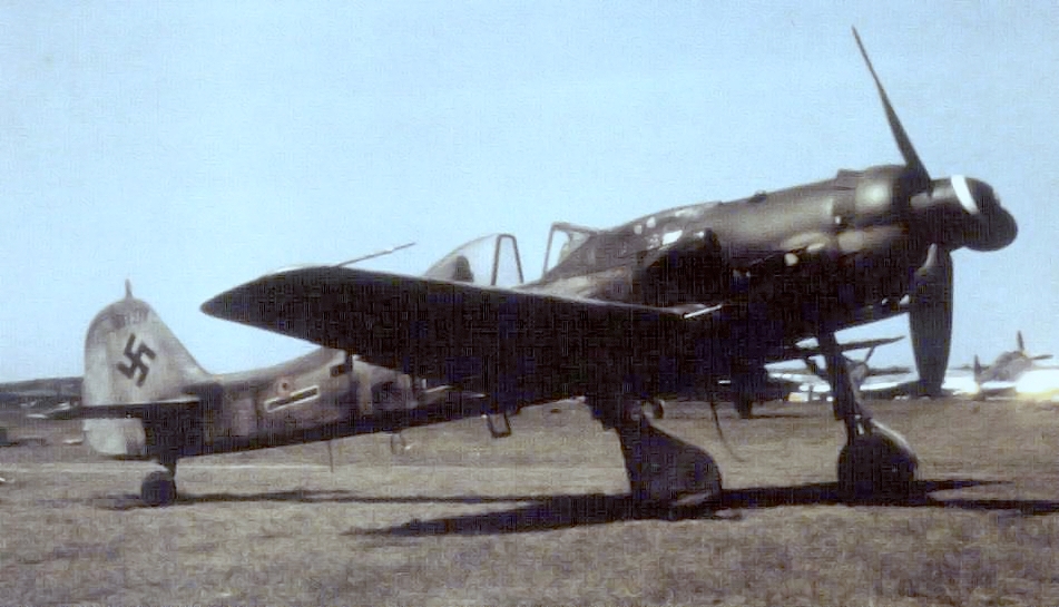 Fw 190 D-9 'Langnasen-Dora' aircraft at rest at an airfield, captured by Americans, post-European War; note P-47 fighters in background