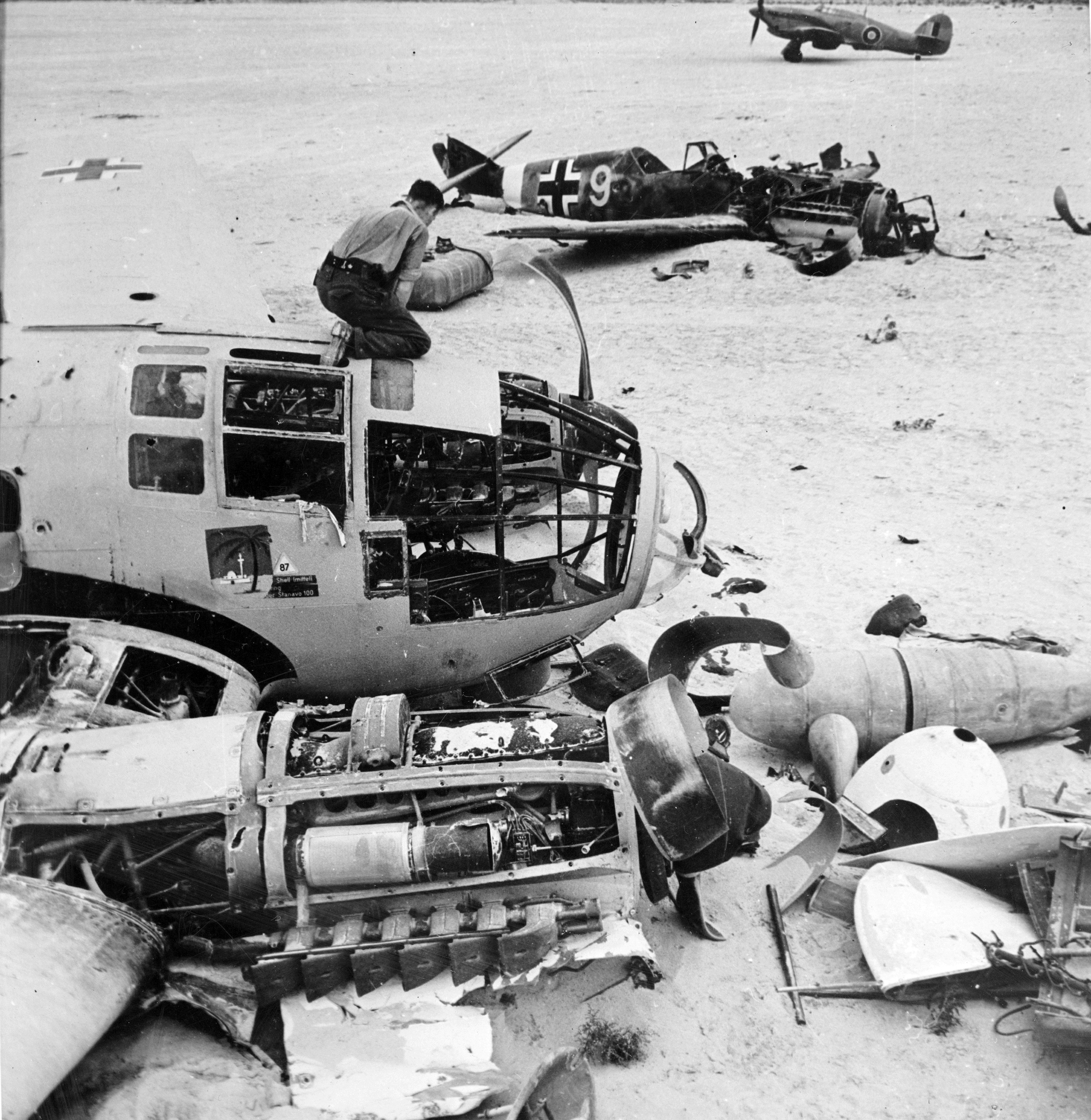 Allied ground crew disassembling a wrecked German He 111 aircraft near Daba and Fuka, Egypt, circa 1942; note wrecked Bf 109 fighter and Hurricane Mk II fighter in background