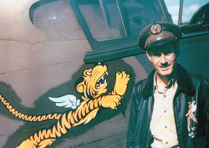 AVG squadron flight leader Robert 'R. T.' Smith standing next to his P-40 Warhawk fighter, Kunming, China, 23 May 1942; note Nationalist Chinese emblem on cap and 'Flying Tigers' emblem on aircraft