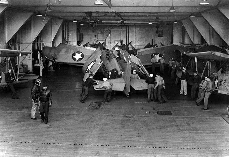 Crewmen spotting F4F-4 Wildcat fighter in Long Island's hangar deck, 17 Jun 1942; note other F4F-4 and SOC-3A aircraft present
