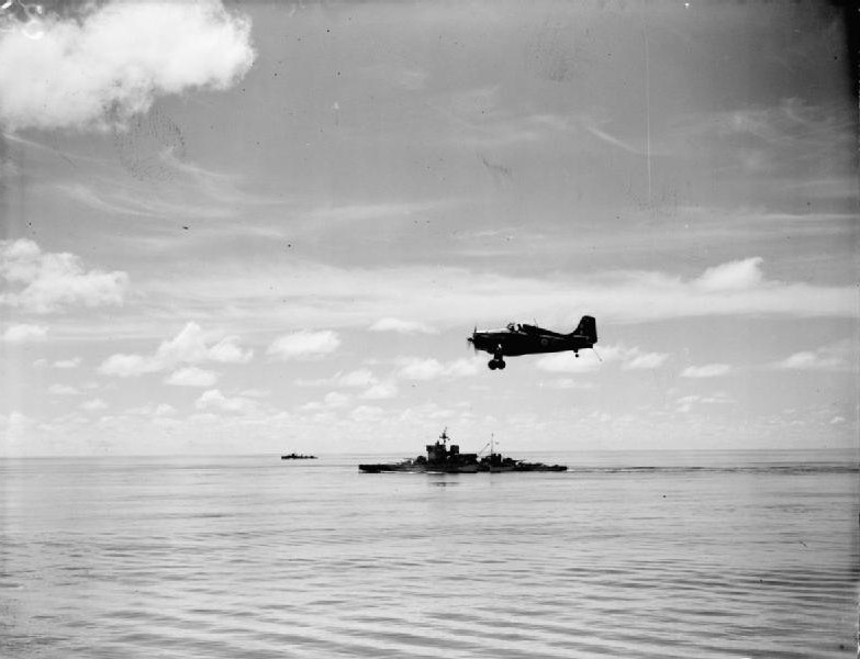 Martlet fighter of No. 888 Squadron FAA from HMS Formidable in flight over the Indian Ocean off Madagascar, late Apr to early May 1942; note HMS Warspite in background